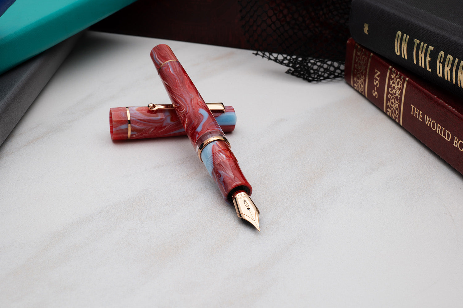 Maroon and gold fountain pen on a marble surface with books in the  background Delta Duna Ghibli Red Fountain Pen lifestyle made in Italy