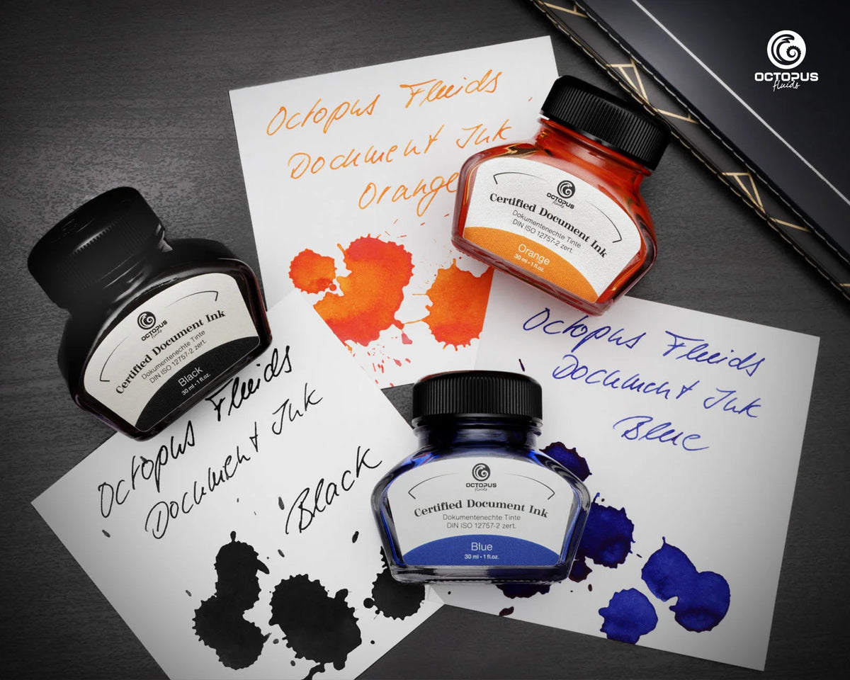 Three Octopus Fluids document ink bottles in black, orange, and blue, arranged on white sheets with ink smears and handwritten text, on a dark textured background. Octopus Fluids Fountain Pen Document Ink - 30 ml Bottle - Dark Blue -  Made in Germany