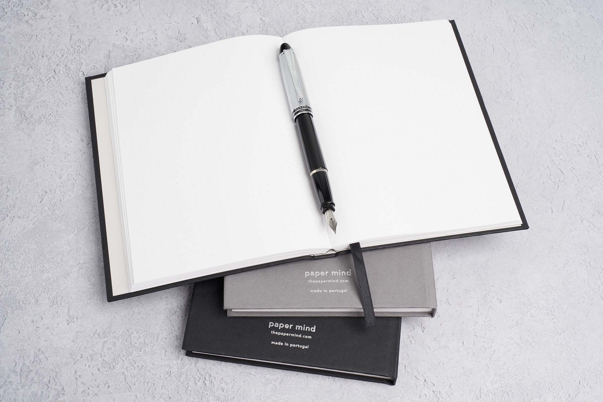 stack of blocker paper notebooks with one laying flat with an aurora ipsilon fountain pen 