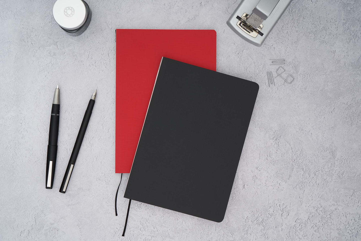 The paper mind Mitsubishi Bank paper notebooks in red and black on gray surface with Lamy fountain pens and ink and a zenith stapler