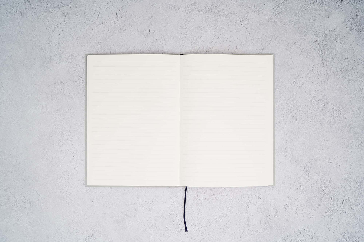 The Paper Mind Cosmo Air Light Hardcover Journal. Fountain pen friendly Journal. Light Gray Japanese Linen Cover. Notebook open ruled on gray concrete background.