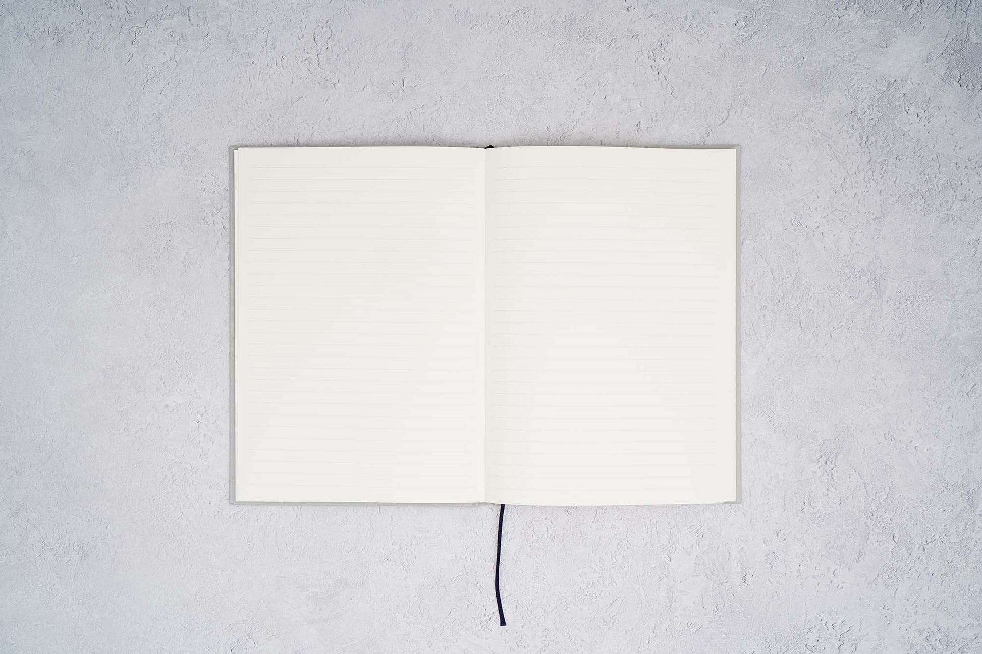 The Paper Mind Cosmo Air Light Hardcover Journal. Fountain pen friendly Journal. Light Gray Japanese Linen Cover. Notebook open ruled on gray concrete background.