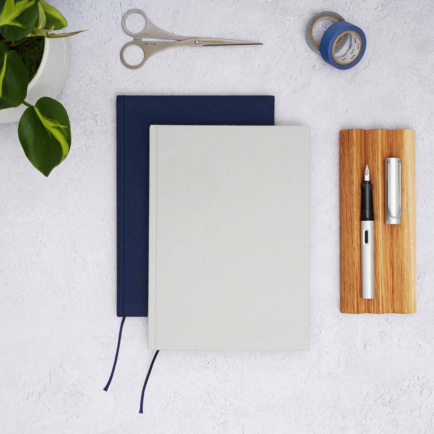 The Paper Mind Cosmo Air Light Hardcover Notebooks in grey and blue with an oak wood pen tray, Lamy AL Star fountain Pen, MT washi tape, Before Breakfast London scissors and plant. Fountain pen friendly notebooks from the paper mind