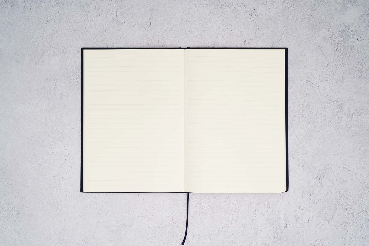 The Paper Mind Passepied Cream Hardcover Notebook. Fountain pen friendly Journal. Navy Blue Japanese Linen Cover. Notebook open with ruled pages on gray concrete background.