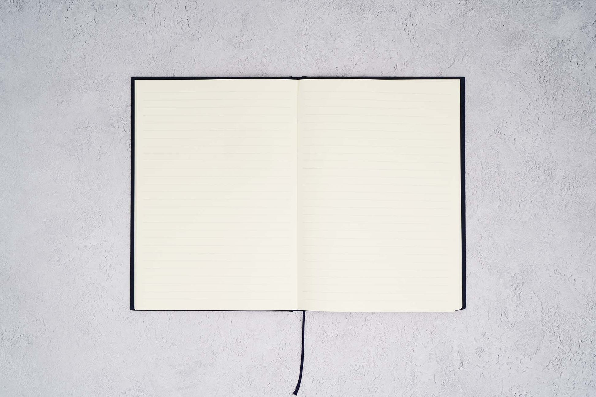 The Paper Mind Passepied Cream Hardcover Notebook. Fountain pen friendly Journal. Navy Blue Japanese Linen Cover. Notebook open with ruled pages on gray concrete background.